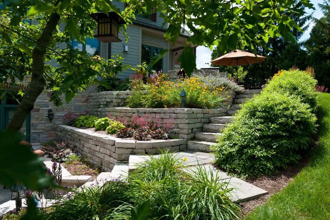 Stone tiered garden beds and staircase leading to a house patio on a sunny day.