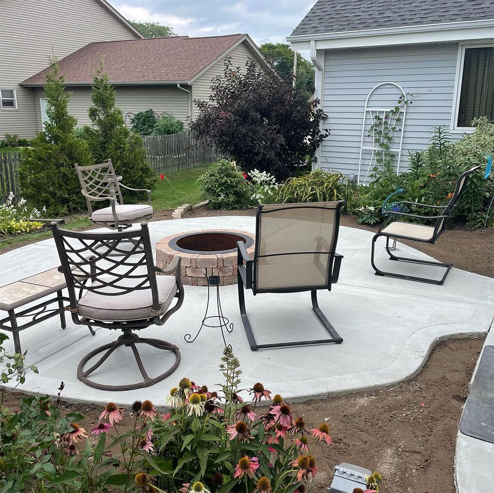 A large stone house with a multi-car garage overlooks a vibrant front garden filled with colorful summer perennials.