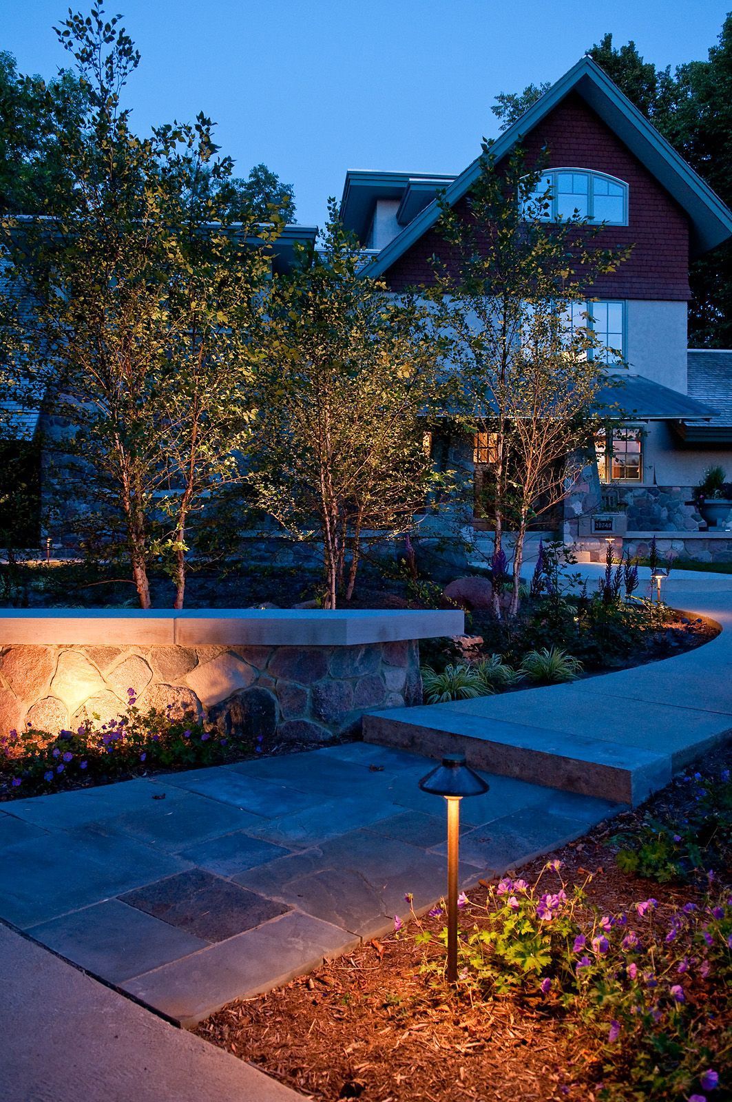 Modern house at dusk with lit garden path, trees, and warm outdoor lighting