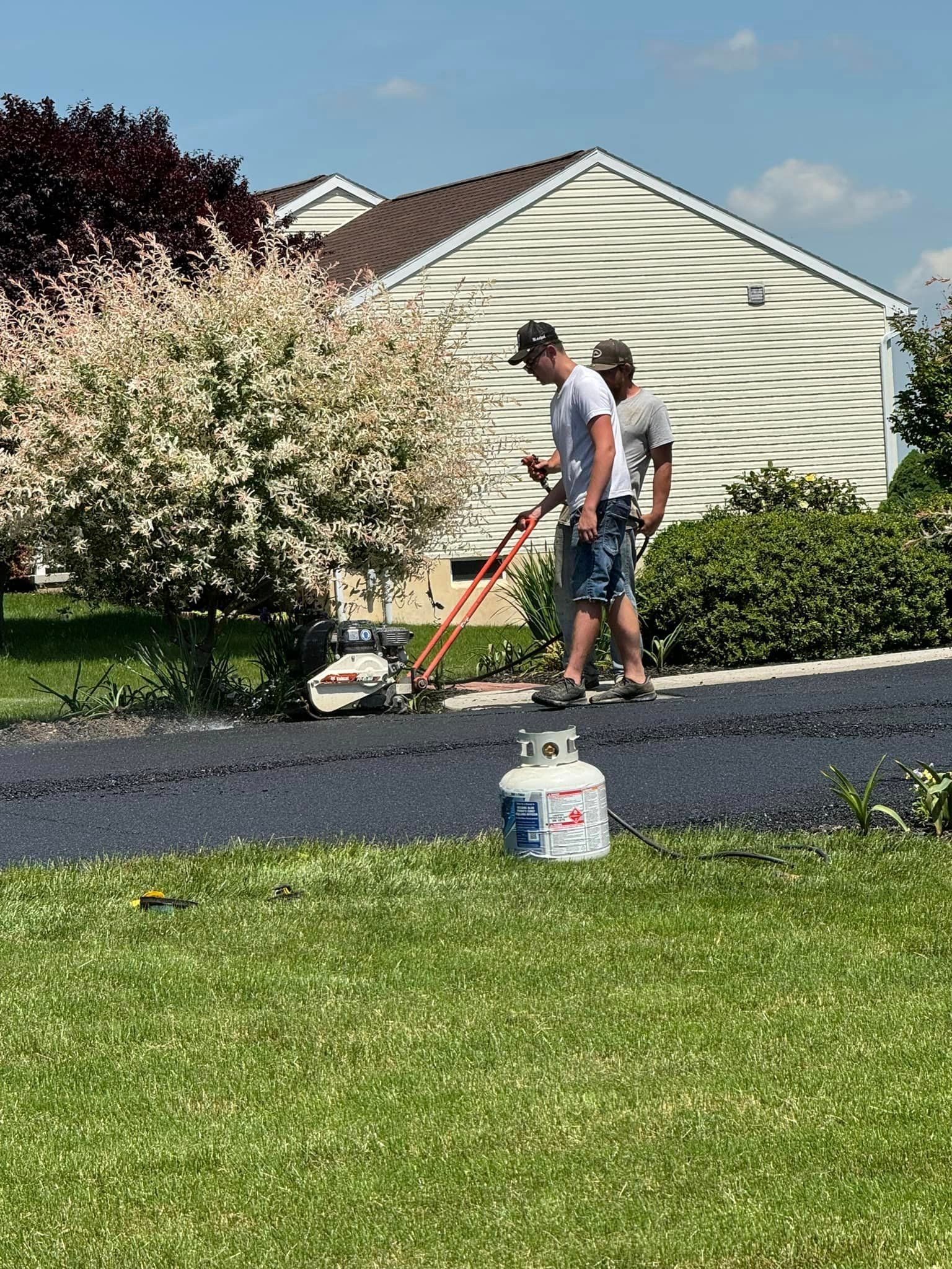 Two men are working on a driveway in front of a house.