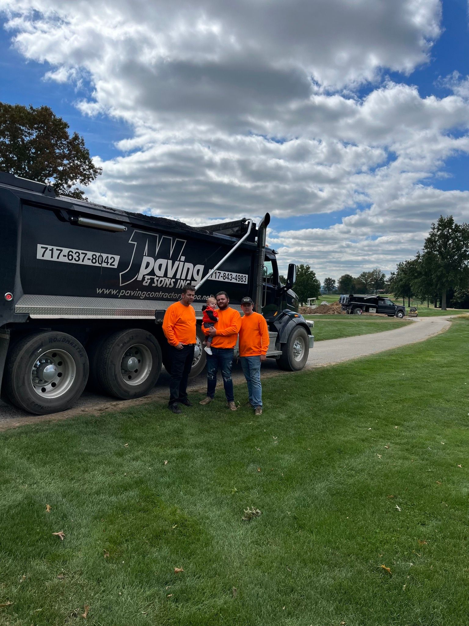 A group of men are standing in front of a paving truck.