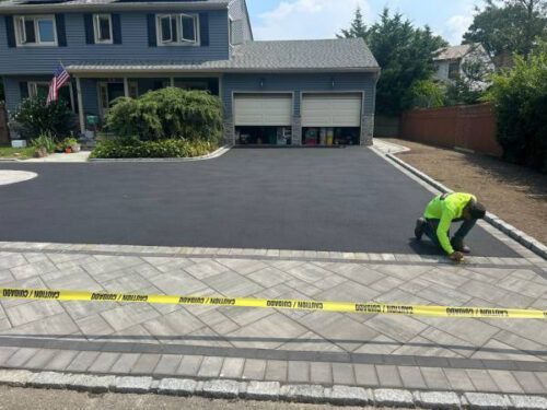 Worker marking asphalt on a driveway in front of a house, with caution tape across the foreground.