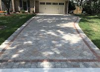 Concrete driveway leading to a garage, bordered by grass and trees in dappled sunlight