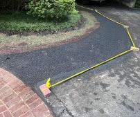 Yellow caution tape blocking a curved asphalt path beside a brick walkway and shrubs