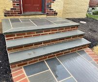 Front steps and porch with gray slate tiles and brick trim leading to a red front door