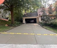 Residential driveway leading to a two-car garage, lined with trees and bushes, with yellow tape across the entrance
