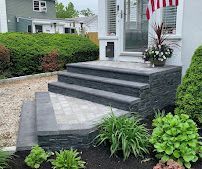 Front porch with dark gray stone steps, paver landing, and potted floral arrangement beside an American flag.