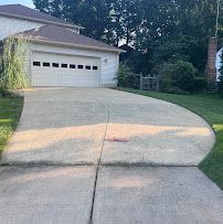 Curved concrete driveway leading to a white garage beside a grassy yard and trees