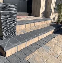 Front steps with gray tile and beige stone paving at a house entrance