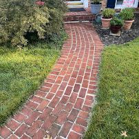 Curved red brick garden path leading to steps, bordered by green lawn and potted plants