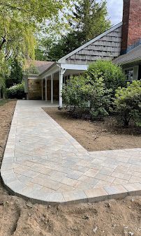 Stone walkway leading to a covered porch beside a brick house and shrubs