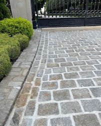 Stone-paved driveway beside trimmed green hedges and a black metal gate