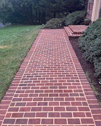 Brick walkway beside a grassy yard and shrubs along a house