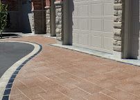 Curved brick walkway beside a beige garage and stone columns in a sunny driveway