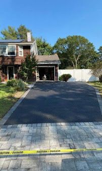 Freshly paved black driveway with gray pavers at a brick house, blocked by yellow caution tape