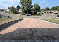 Brick walkway leading to a suburban street with trees, parked cars, and houses under a clear blue sky