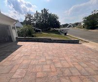 Brick-paved driveway beside a suburban street and lawn under a bright sky