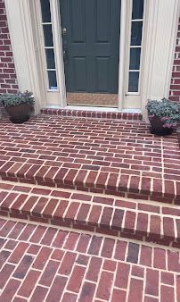 Brick front steps leading to a dark front door with potted plants on either side