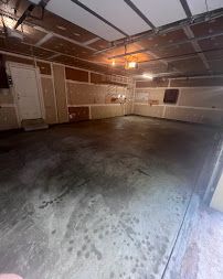 Empty garage with a wet concrete floor, beige walls, and the door open to daylight.