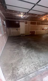 Empty garage with concrete floor, wood-paneled walls, and a closed door under a partially open garage door.