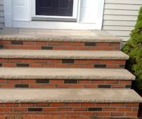 Brick front steps leading to a white door with black window and beige siding