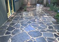Stone-paved walkway beside a building, with irregular dark gray stones outlined in white mortar.