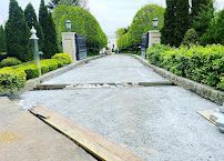 Broken driveway at a landscaped entrance with trimmed hedges and stone gateposts, viewed from the road