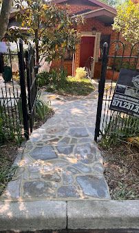 Stone walkway leading to a red-brick house behind a black metal gate and garden plants