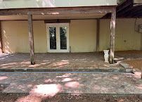 Covered patio with wooden posts, white double doors, and a stone walkway in front of a beige building