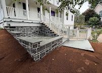 House front with a terraced stone stairway and unfinished wire-frame retaining wall on a sloped yard