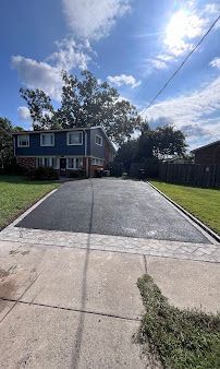 Residential driveway with a gravel center, concrete edges, lawn, and a two-story house under a blue sky