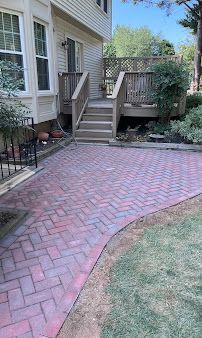 Brick patio walkway leading to wooden steps and a house entrance, with a small lawn beside it
