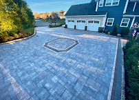 Large gray paved driveway with a central diamond pattern in front of a house and garage at sunset