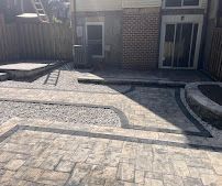 Stone patio in front of a brick house, with curved paving patterns and steps leading to the entrance.