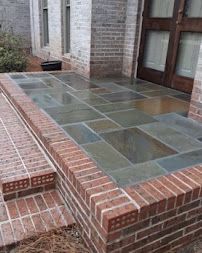 Brick patio with large slate pavers beside a house, bordered by low brick walls and steps
