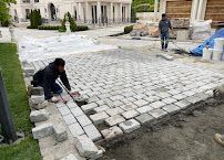 Workers laying light gray cobblestones in a courtyard with classical buildings in the background