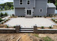 Backyard stone patio with steps, retaining walls, and a gray house overlooking a lake