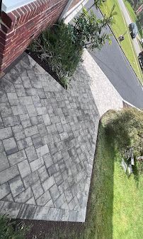 Paved front walkway and driveway beside a brick house, with shrubs and green lawn.