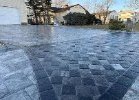 Textured blue-gray paver driveway with a house and trees in the background