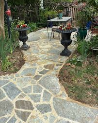 Stone garden path leading to a small patio table with potted plants and decorative urns
