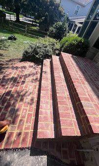 Brick steps leading to a grassy yard with bushes and a house porch in the background