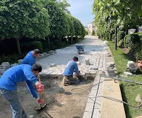 Workers in blue uniforms repairing a concrete path beside a tree-lined canal