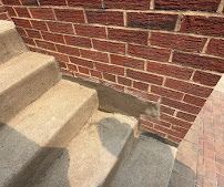 Concrete steps beside a red brick wall with a visible patch of repair work