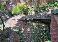 Backyard garden with a gravel path, brick wall, and low wooden retaining wall by plants and a fence