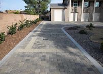 Paved driveway with a curved border leading to a garage beside a modern house in a desert landscape