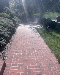 Sunlit red brick walkway bordered by green grass and shrubs