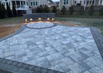 Stone patio with built-in fire pit in a backyard, lit with warm lights at dusk