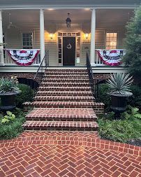 Brick house porch with white columns, striped bunting, and a wide staircase leading to the front door
