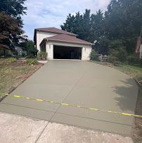 Long concrete driveway leading to an open garage beside a house, with trees and greenery around it