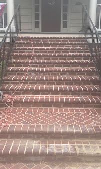Brick front steps leading to a house entrance with white railings and a dark door